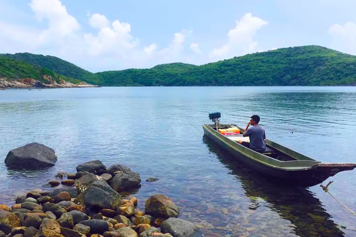 Traveler sitting in the boat in the calm waters of Dam Tre Bay surrounded by mountains